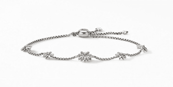 The PETITE STARBURST BRACELET is a delicate, silver accessory featuring a thin chain with a sliding clasp adorned with a small, circular detail. Along its length are several evenly spaced charms that resemble small starbursts.