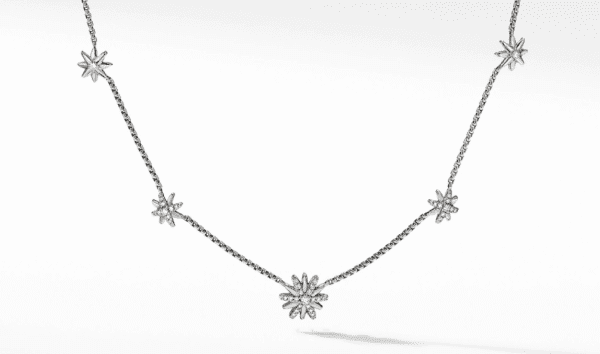 The STARBURST STATION NECKLACE is a delicate silver necklace featuring five evenly spaced, star-shaped pendants along its chain. The stars are symmetrical and elegantly crafted, adding a touch of sparkle and sophistication to the simple design of the necklace.