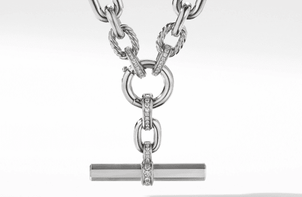 A close-up image of the LEXINGTON DIAMOND LINK CHAIN, a silver necklace with large interlocking chain links. The necklace features a toggle clasp with a horizontal bar and round links, some of which are adorned with small, sparkling crystals. The background is a smooth white surface.