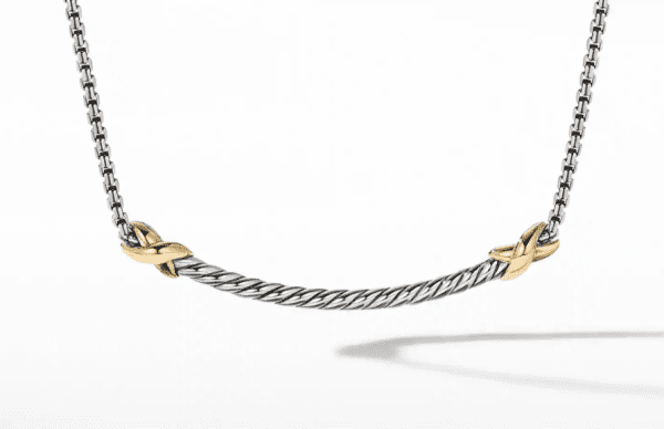 A close-up image of the PETITE X BAR NECKLACE featuring a twisted silver cable design with two gold X-shaped accents. The necklace has a delicate chain and a sleek, modern appearance, with a minimalist background that highlights its elegant details.