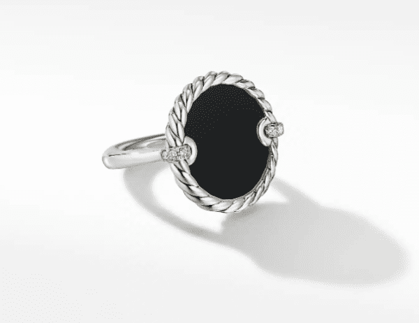 The 18MM ELEMENTS RING features a silver band adorned with an oval black onyx centerpiece, surrounded by a twisted rope design. On either side of the onyx, two small accent stones that resemble diamonds are set. The ring casts a soft shadow against a white background.