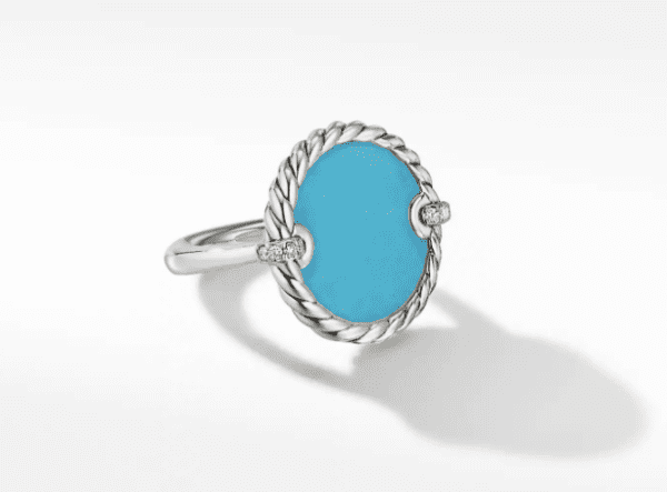 The 18MM ELEMENTS RING features a large, oval turquoise stone set in the center, secured by four small clasps adorned with sparkling diamonds. The band has a simple twisted rope design surrounding the stone.