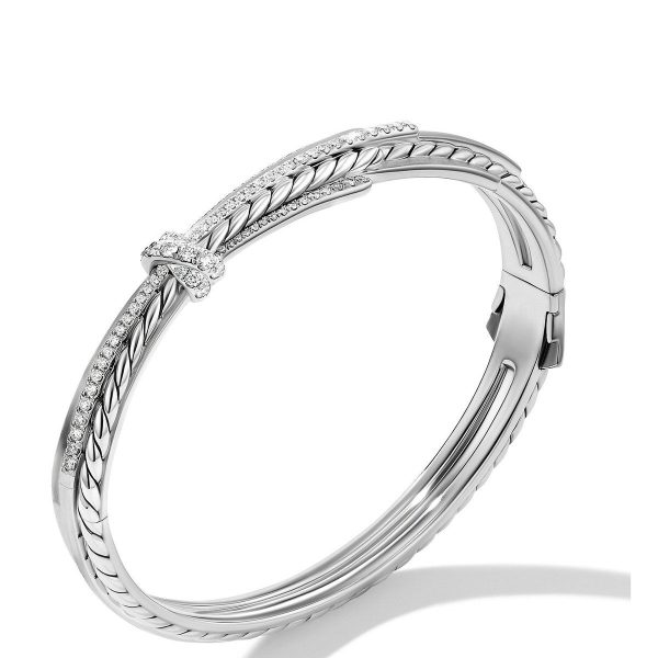 The ANGELIKA BRACELET is a sleek silver accessory designed with a twisted rope-like pattern, adorned with a small cluster of sparkling diamonds at the top. It features a hinged clasp mechanism for easy wearing.