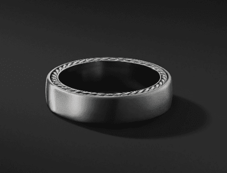 The 6MM Streamline Band, featuring intricate braided detailing along the edge, rests on a smooth, dark background. This sleek silver ring has a modern, polished look with a subtle yet elegant design.