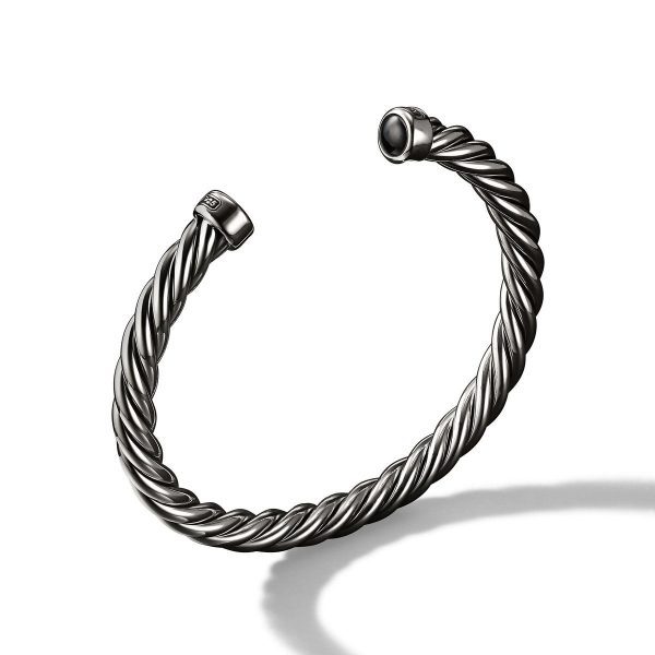 The 6MM CABLE CLASSIC CUFF is a silver twisted cable bracelet with open ends, each tipped with a small, round, dark stone. The cuff casts a shadow on a white background, highlighting its elegant and minimalistic design.