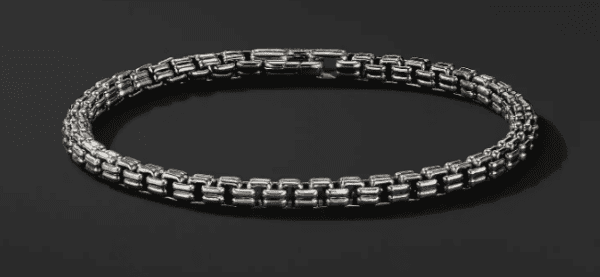 A close-up of the 4MM DOUBLE BOX CHAIN is shown against a black background, highlighting its intricate interlocking rectangular link design. The silver chain appears sleek and polished, emphasizing its detailed craftsmanship.