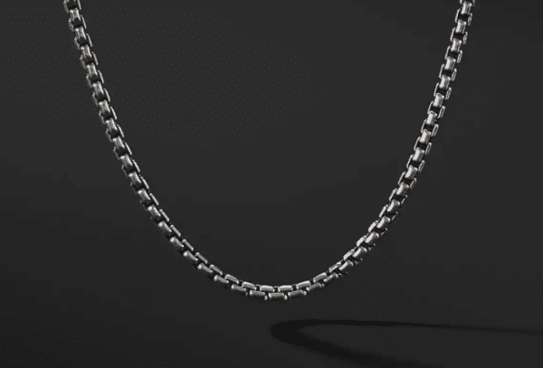 A close-up of the 2.7MM MENS BOX CHAIN against a black background, showcasing its intricately detailed links and sleek, polished surface. The chain curves gently, casting a subtle shadow beneath it.