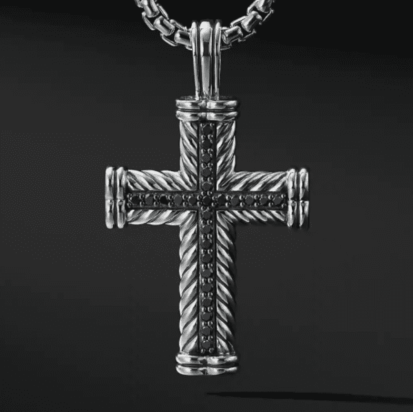 Close-up of the PAVE CROSS ENHANCER, showcasing its intricate rope-like detailing and central design adorned with black gemstones. The silver cross hangs from a thick, round-link silver chain against a solid black background, highlighting the pendant's exquisite design.