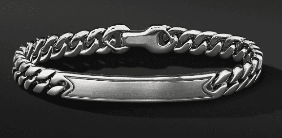 A close-up image of the 8MM CURB CHAIN IDENTIFICATION bracelet featuring thick, interlocking silver links and a polished blank plate at the center. The bracelet is securely clasped and set against a dark, smooth background, which accentuates its metallic sheen and intricate craftsmanship.