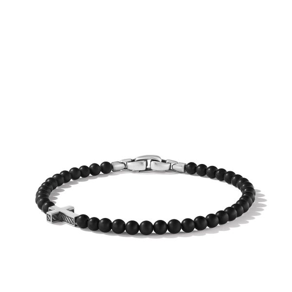 The 4MM CROSS STATION BEAD BRACELET BO showcases a minimalist design with small round black beads strung together and secured with a silver-toned clasp. An off-center silver cross detail adds a unique touch to the bracelet, which is displayed on a white background.