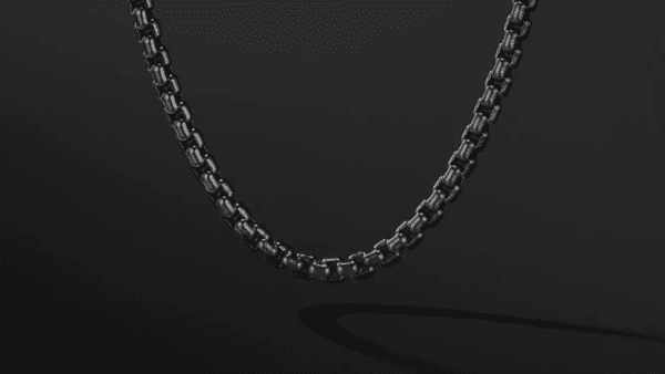 The 4MM BOX CHAIN BLK SANDBLAST is evenly illuminated and showcased against a dark backdrop. The chain's box-shaped links are interlocked, forming a seamless, sophisticated design. A subtle shadow of the necklace can be seen beneath it.