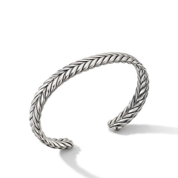 The 9MM Chevron Cuff Bracelet is a silver open cuff with a sleek, twisted design. Its polished finish enhances the intricate chevron pattern, casting a subtle shadow on the white surface beneath it.