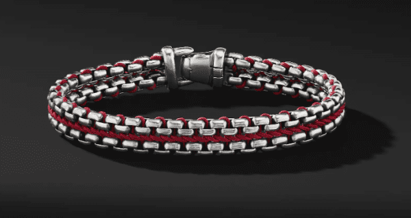 The 12MM Woven Box Chain showcases a sleek double-strand design with interwoven silver metal links and red threads, all clasped together with a polished silver closure, beautifully displayed against a dark background.