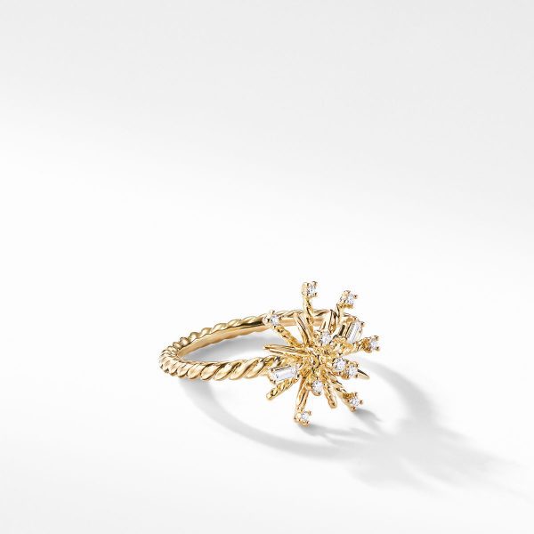 The 14MM SUPERNOVA RING showcases a twisted band design in gold, adorned with a starburst-shaped cluster of small diamonds at its center. The ring is elegantly presented on a white surface, casting a soft shadow.