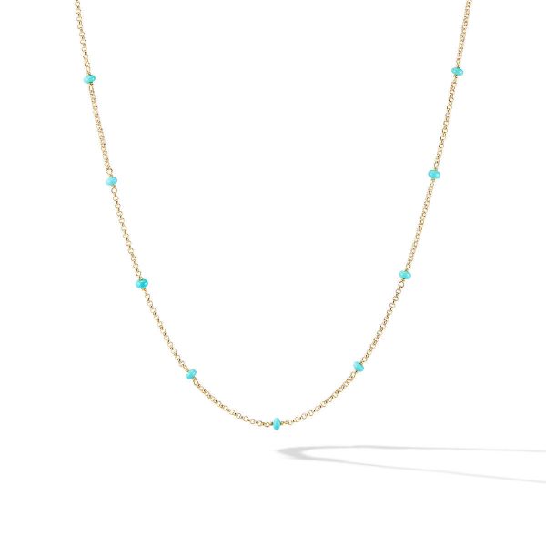 The COLLECTIBLE BEAD AND CHAIN NECKLACE TQ features a delicate gold chain adorned with small, evenly spaced turquoise beads. It is showcased against a white background, with a faint shadow cast below.