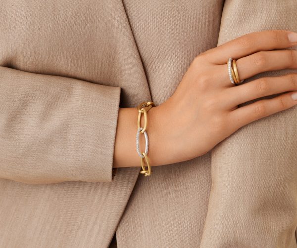 A person in a beige blazer crossing their arms, wearing a Marco Bicego Jaipur Oval Link and Diamond Bracelet alongside a gold ring on their finger.