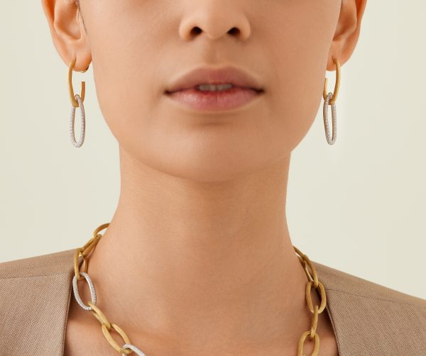 A person wearing Marco Bicego Jaipur Diamond Drop Earrings with a silver oval pendant and a gold chain necklace, set against a soft, neutral background.