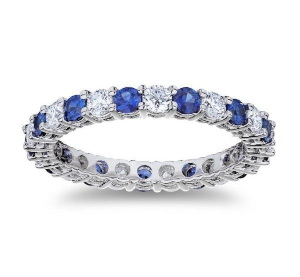 The Bromberg's Signature Collection Sapphire and Diamond Eternity Band is a silver ring featuring alternating round-cut blue sapphires and clear diamonds set in a continuous band, creating a sparkling effect. The ring is displayed against a white background.