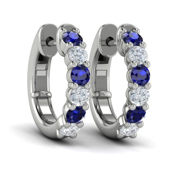 The Vlora Sapphire and Diamond Hoop Earrings are an elegant pair of hoops adorned with alternating blue sapphires and white diamonds set in polished silver. The gemstones are arranged in a line, creating a symmetrical and sparkling design.