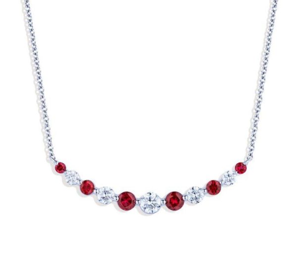 The Bromberg's Signature Collection Ruby and Diamond Necklace is a delicate silver piece, featuring a symmetrical arrangement of alternating round red rubies and white diamonds. The stones are set in a descending size pattern, with the largest stones in the center gradually decreasing in size towards the ends.