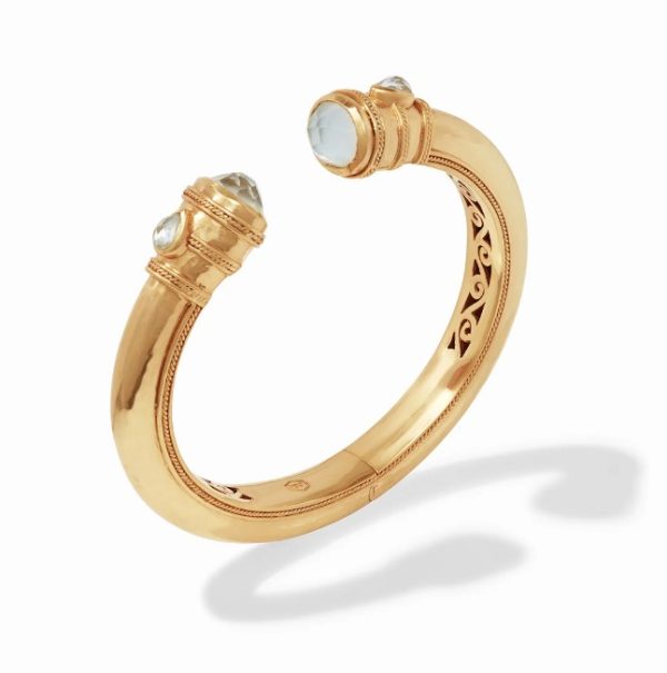 The Julie Vos Cannes Demi Cuff is a gold cuff-style bracelet with intricate detailing along its length. The bracelet ends in two ornate, cylindrical caps, each adorned with a clear gemstone. The design includes fine engravings and a smooth polished finish, casting a shadow on a white background.