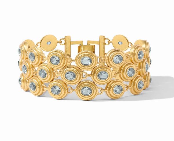 The Julie Vos Tudor Triple Row Tennis Bracelet showcases a gold bracelet with multiple rows of round blue gemstone settings. It features a wide, symmetrical design where each gemstone is encased in a circular gold bezel. The prominent clasp blends seamlessly with the intricate detailing of the bracelet.