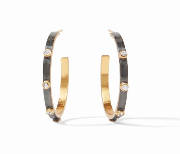 The Julie Vos Crescent Stone Hoop Earrings feature a pair of open hoops with a striking two-tone design. The outer side is dark grey, embellished with small diamond-like stones evenly spaced around the hoop, while the inner side boasts a polished gold finish. The earrings cast elegant shadows against a white background.