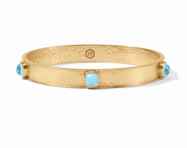 The Julie Vos Catalina Stone Bangle in Iridescent Capri Blue is a textured gold bracelet with three turquoise gemstone accents spaced evenly around the band. The bracelet also features a small hexagonal emblem, which can be engraved with an initial or symbol.