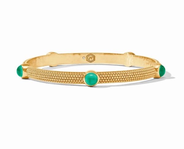 The Julie Vos Cabochon Bangle Bracelet in Iridescent Emerald Green boasts a gold bangle design with a textured surface adorned with evenly spaced emerald green gemstone accents. Inside, the bracelet features an engraved logo and is beautifully showcased against a white background.