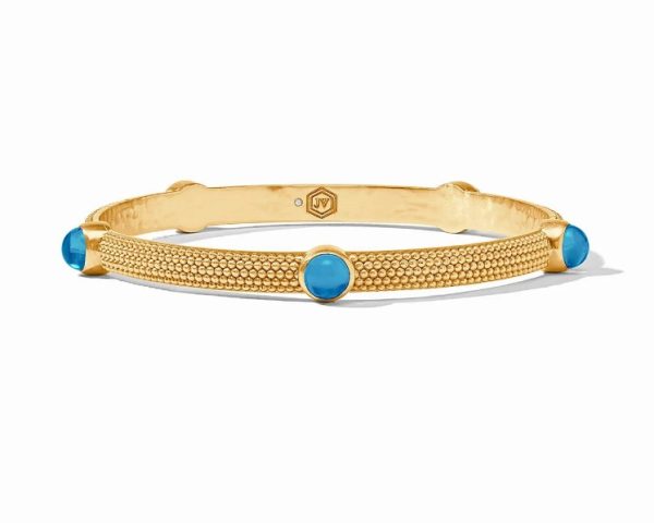 The Julie Vos Cabochon Bangle Bracelet in Iridescent London Blue showcases a textured gold band adorned with four evenly spaced, round turquoise stones. This bangle boasts a subtle shine and an elegant, minimalist design.