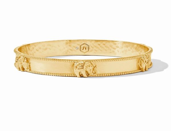 The Julie Vos Elephant Bangle Bracelet is a gold bangle adorned with small elephant motifs evenly spaced along the band. The inner side has a subtle texture and features a small logo with the initials "JV". The edges are slightly beaded, adding detail to its design.