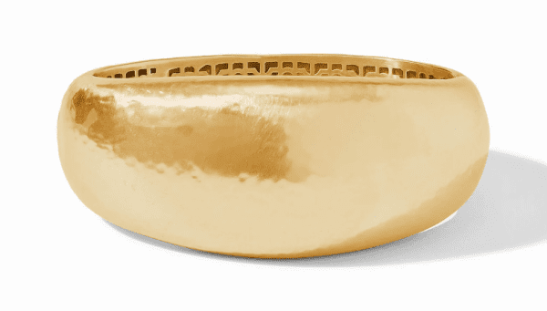 The Julie Vos Catalina Statement Hinge Bangle Bracelet is a stunning piece featuring a shiny, hammered gold finish with a smooth, curved outer surface and an intricate openwork pattern on the inner side. The bracelet's polished and reflective finish bestows an elegant and luxurious appearance.