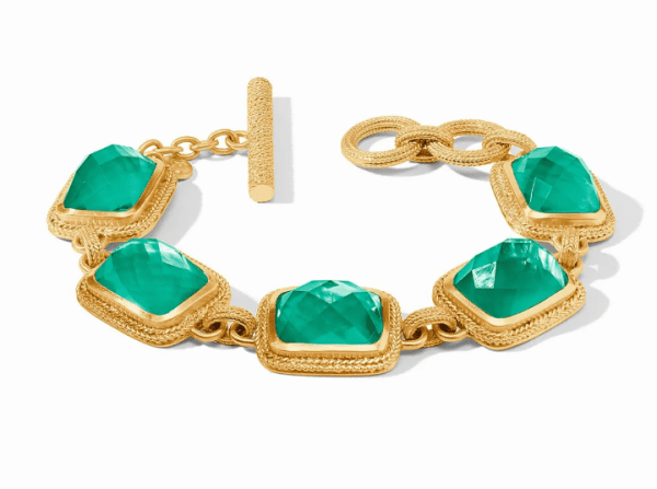 The Julie Vos Cheval Stone Bracelet in Iridescent Emerald Green features five square emerald-green gemstones, each framed in a detailed gold setting and secured with a textured toggle clasp.