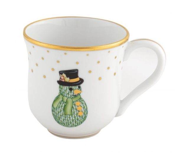 The Herend Holiday Mug - Snowman is a white ceramic mug with a handle, adorned with gold-rimmed edges and gold polka dots. It features an image of a green, cross-hatched snowman sporting a black hat and scarf, giving it a festive and playful design.