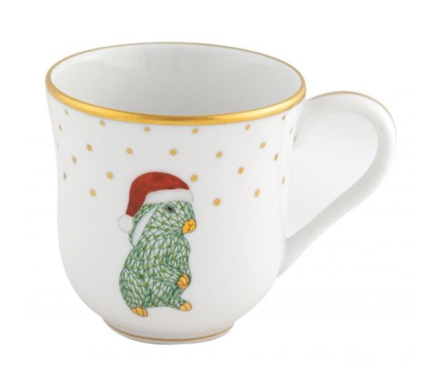 The Herend Holiday Mug - Santa Bunny is a white ceramic mug adorned with gold trimming on both the rim and handle. It features a charming pattern of small gold dots and an illustration of a green rabbit wearing a red and white Santa hat.