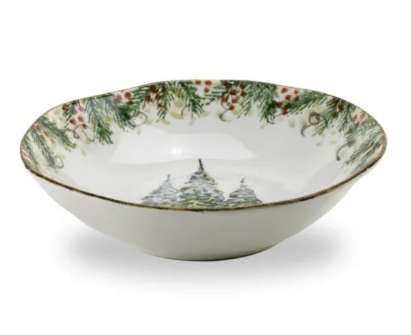 The Arte Italica Natale Pasta/Soup Bowl is a shallow ceramic dish decorated with a charming winter motif. The rim showcases a festive pattern of pine branches, ribbons, and red berries, while the center features a trio of snow-covered evergreen trees. It also boasts a wavy, slightly irregular edge for added character.