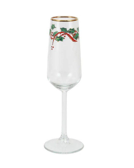 The Vietri Holly Champagne Flute, featuring a festive design of holly leaves, red berries, and a red ribbon on a clear glass with a gold rim, stands empty against a plain white background.