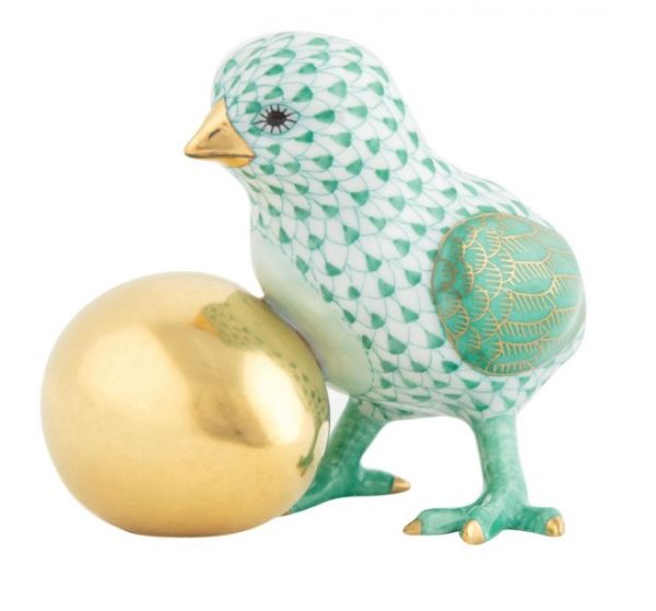 The Herend Baby Chick with Egg Figurine in Green features a porcelain bird adorned with a green and white diamond pattern and gold accents, standing next to a shiny golden orb. The figurine boasts intricate details, including delicate feather patterns and bright eyes. The overall design is both elegant and whimsical.