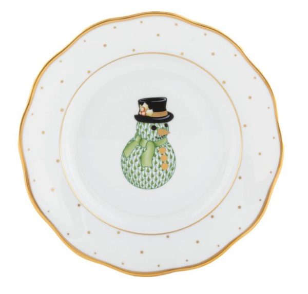 The Herend Holiday Dessert Plate - Snowman showcases a decorative white design with a scalloped edge accented by a gold trim. At its center is an illustration of a green snowman wearing a black top hat adorned with a flower, and the border is elegantly patterned with gold dots.