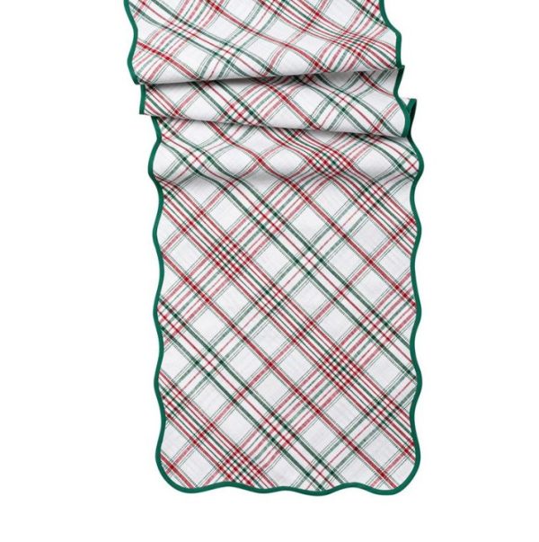 A folded Juliska Merry Tartan 18" x 90" table runner featuring a green, red, and white plaid pattern is displayed. The runner showcases scalloped edges trimmed in green.