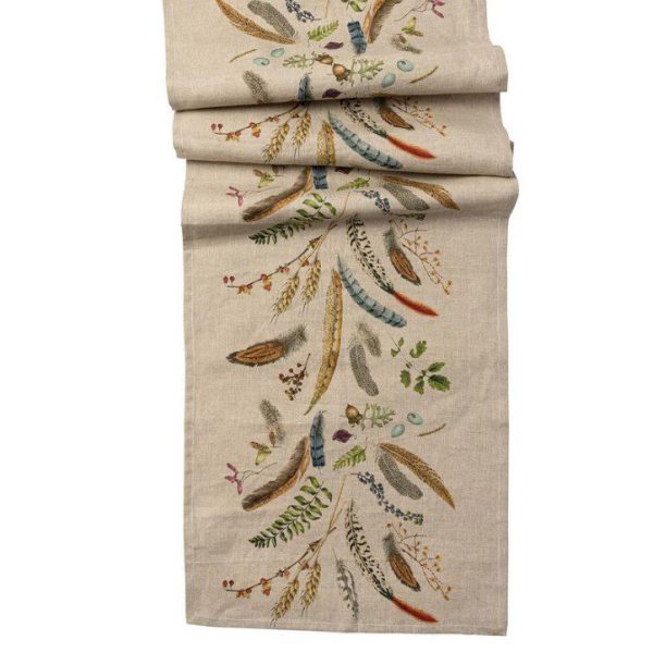 The Juliska Forest Walk 18" x 90" Table Runner, draped in folds, features an intricate embroidered pattern of colorful feathers, leaves, branches, and berries. The design blends natural elements in earthy tones, creating a nature-inspired decorative piece.