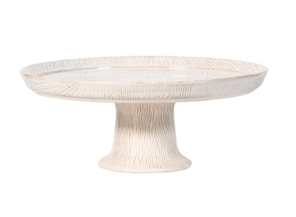 The Juliska Blenheim Oak Cake Stand - Whitewash is a ceramic cake stand featuring a textured surface that mimics the natural grain of wood. It has a wide, fluted base that supports the round, flat top, perfect for showcasing cakes or other baked treats. The stand boasts a soft off-white color with delicate light brown accents.