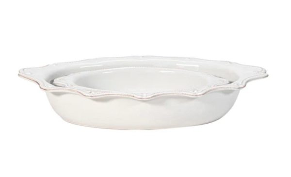 The Juliska Berry & Thread Oval Baker Set in Whitewash features a white, oval-shaped ceramic serving dish with decorative, scalloped edges. This dish boasts a glossy finish and intricate detailing along the rim, making it an elegant choice suitable for formal dining occasions.