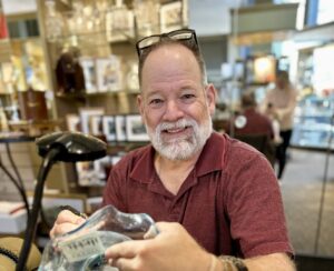 Master Engraver at Bromberg’s in Birmingham, AL, smiles while engraving a crystal vase at his workstation.