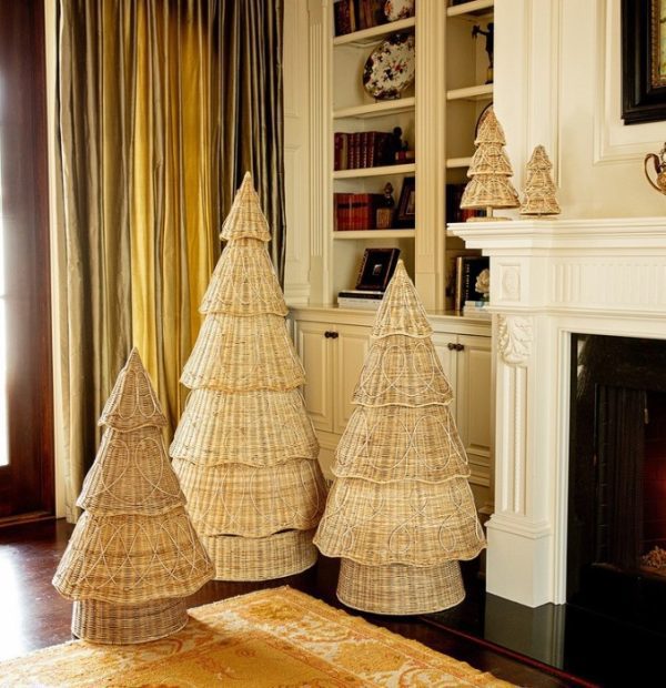 A room with Juliska Provence Rattan Trees - 4 ft in various sizes placed near a white fireplace mantel. There are built-in shelves on the wall holding books and decorative items, and floor-to-ceiling curtains next to a wooden door. A yellow and white rug adorns the floor.