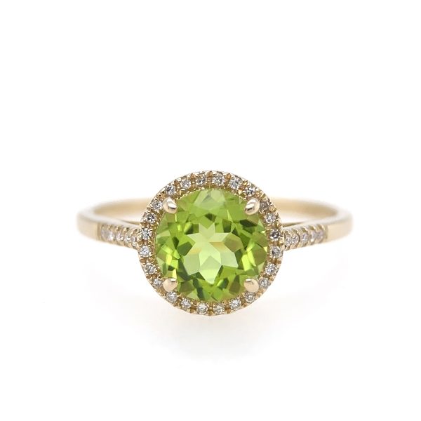 The Bromberg's Signature Collection Peridot and Diamond Ring showcases an elegant design with a large, round peridot gemstone at the center, encircled by a halo of smaller, sparkling white diamonds. The band is further adorned with small diamonds on each side of the centerpiece, enhancing its luxurious appearance.