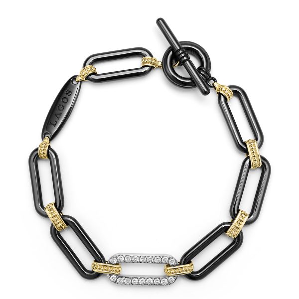 The LAGOS Signature Caviar 18K Gold and Black Ceramic Diamond Station Link Bracelet is an elegant piece with large, black rectangular links combined with smaller, textured gold links. One of the links is adorned with shimmering diamonds. The bracelet features a toggle clasp and a black engraved tag displaying the brand name "LAGOS".