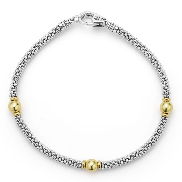 The Signature Caviar Two-Tone Station Bracelet is a silver beaded bracelet featuring intricate detailing, a lobster clasp, and three gold spherical beads evenly spaced along the design.