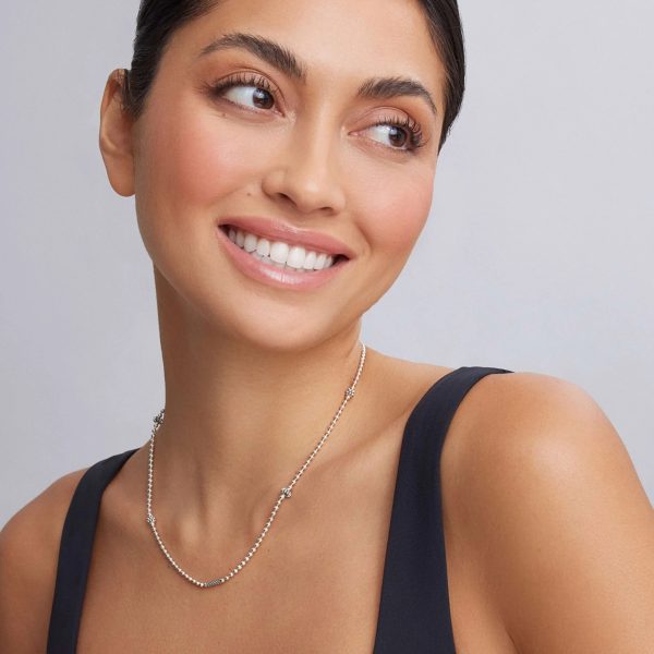 A woman with dark hair is smiling and looking to the side. She is wearing a sleeveless black top and the LAGOS Caviar Icon Silver Caviar Beaded Necklace. The background is a simple light gray.