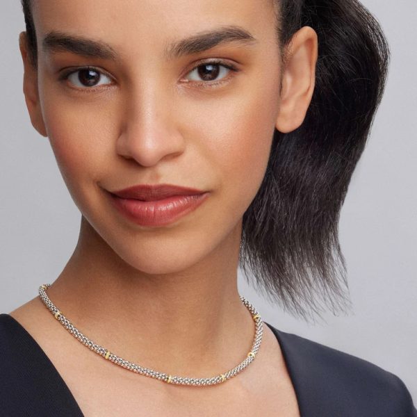 A woman with dark hair styled in a ponytail, wearing a natural makeup look, smiles subtly for the camera. She is dressed in a black top and the LAGOS Signature Caviar Two-Tone Caviar Beaded Necklace, set against a plain background.